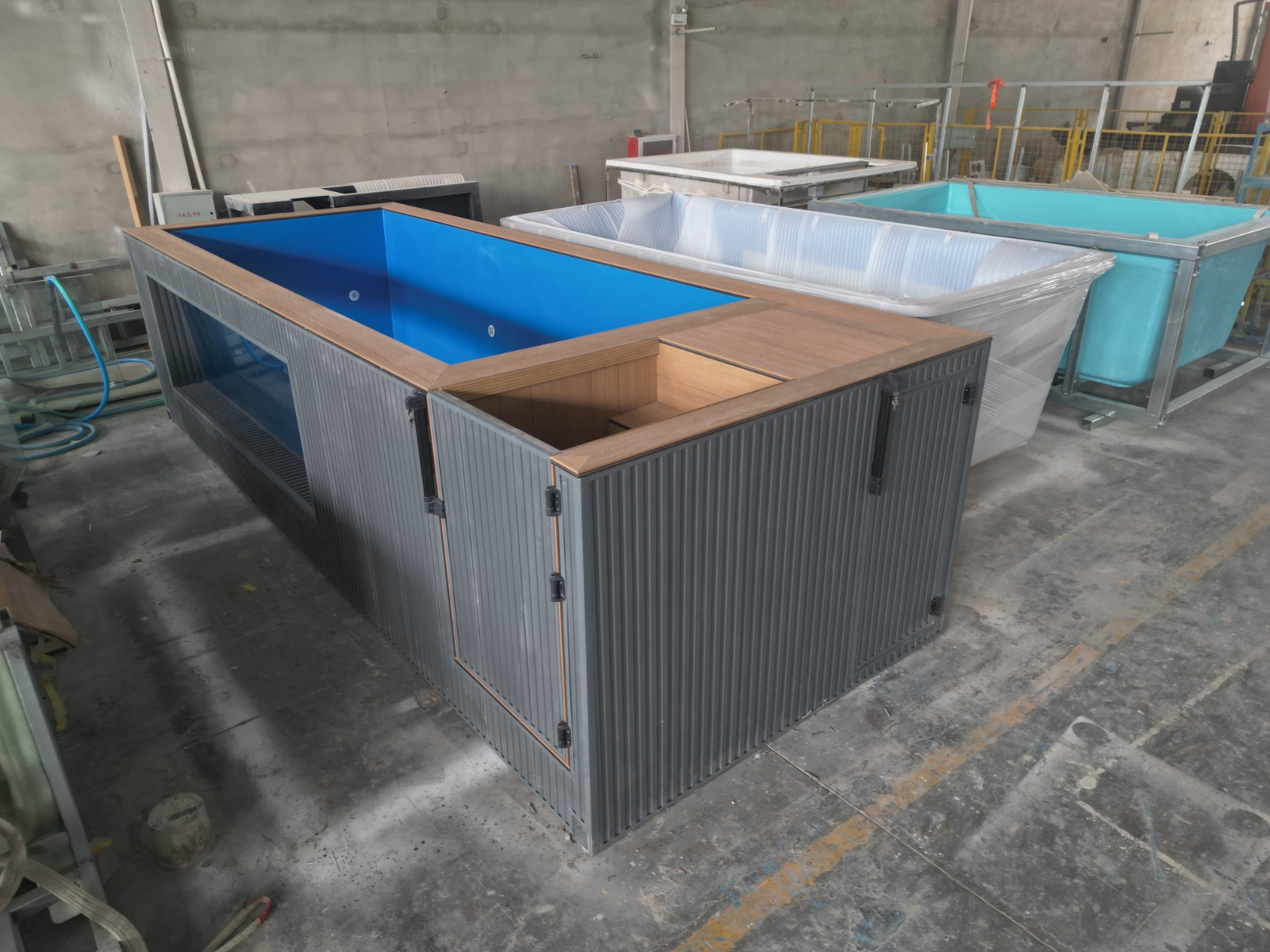 Real 20ft glass-side pool in the factory, with grey cladding, timber-toned WPC surround and blue fibreglass interior